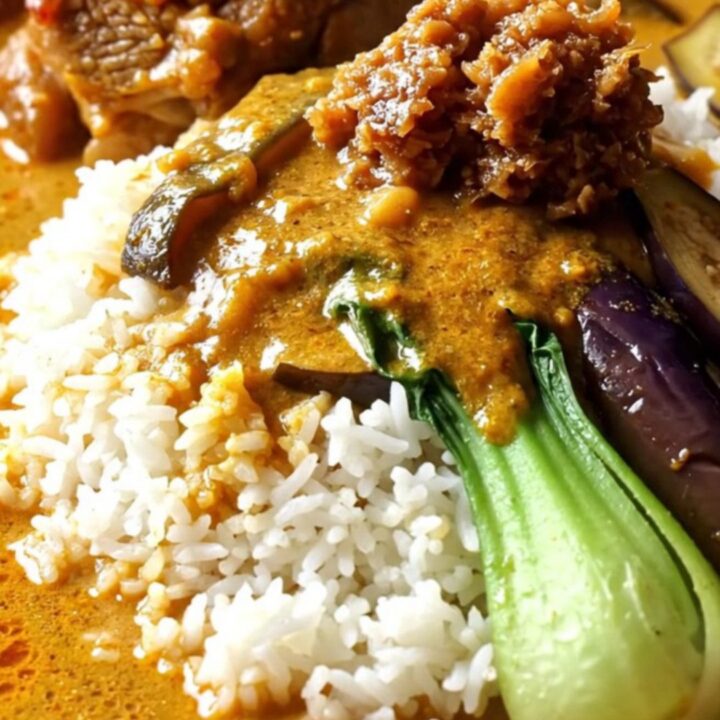 Close-up of golden-orange Filipino Kare-Kare with oxtails and vegetables in a ceramic Crockpot.