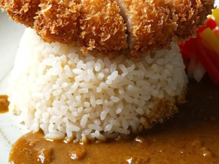A close-up of a dark ceramic bowl filled with rich Japanese golden beef curry and tender vegetables.
