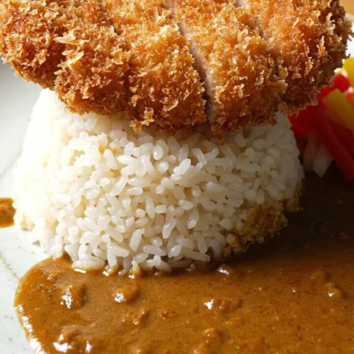 A close-up of a dark ceramic bowl filled with rich Japanese golden beef curry and tender vegetables.