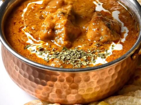 A close-up of a copper pot filled with rich, creamy orange butter chicken with tender pieces of chicken.
