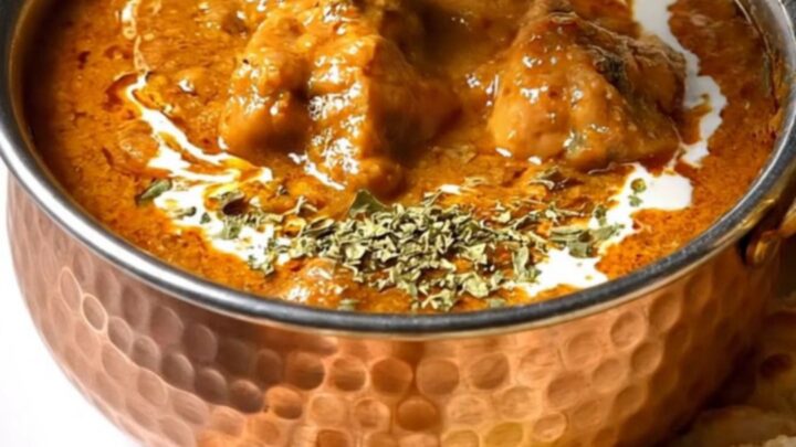A close-up of a copper pot filled with rich, creamy orange butter chicken with tender pieces of chicken.