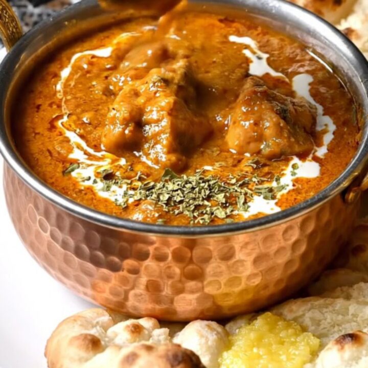 A close-up of a copper pot filled with rich, creamy orange butter chicken with tender pieces of chicken.