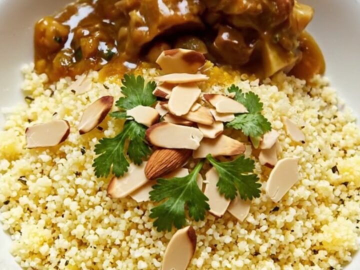 A close-up of a Moroccan lamb tagine in a yellow ceramic pot, garnished with cilantro and toasted almonds.