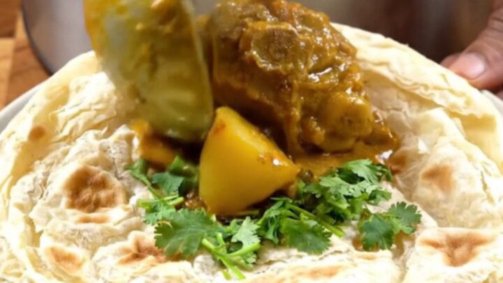 A steaming bowl of authentic Trinidadian curry goat with tender meat, potatoes, and a rich gravy.