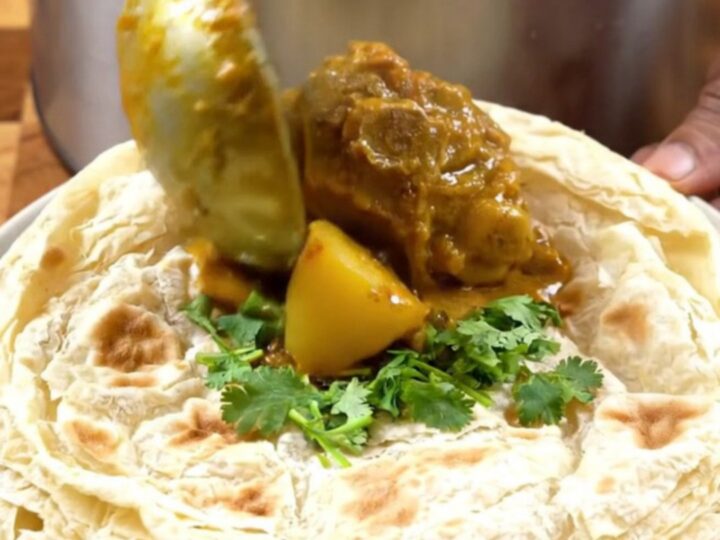 A steaming bowl of authentic Trinidadian curry goat with tender meat, potatoes, and a rich gravy.