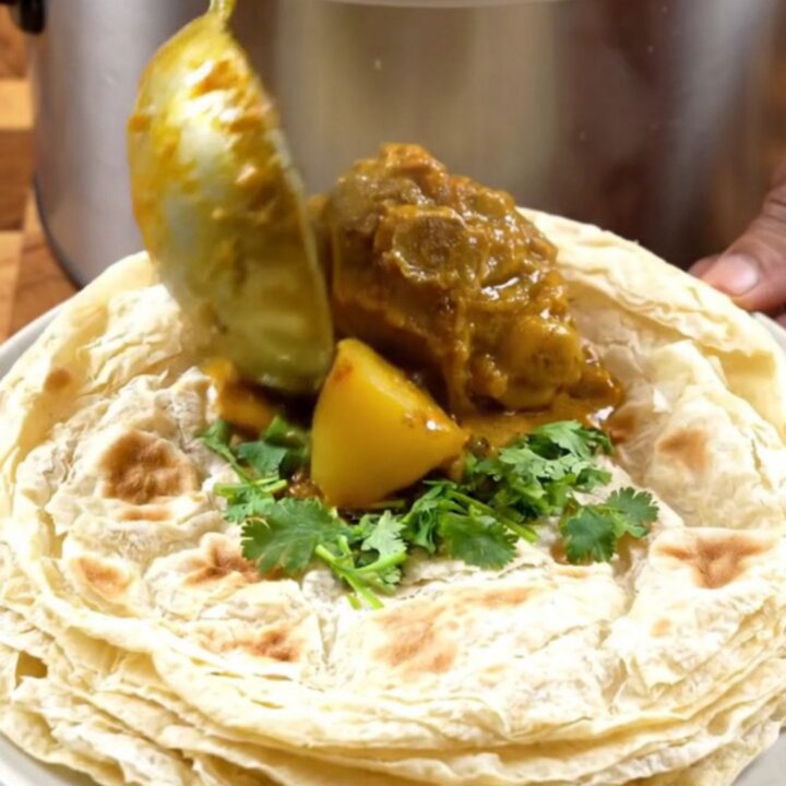 A steaming bowl of authentic Trinidadian curry goat with tender meat, potatoes, and a rich gravy.