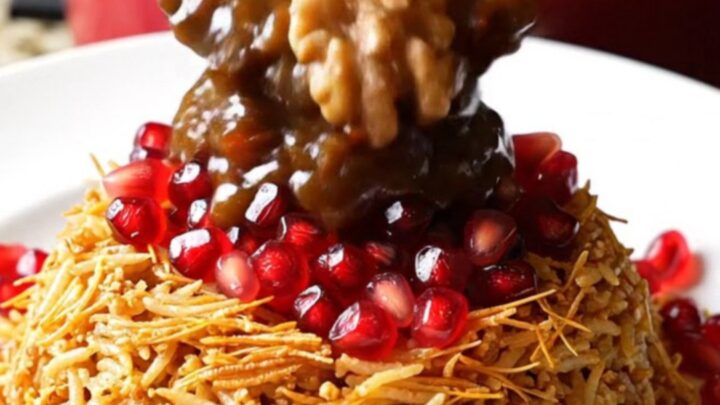 A close-up of a mahogany-colored Persian Fesenjan stew served in a pomegranate-red ceramic crockpot.