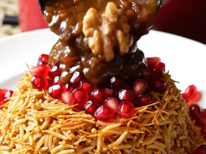 A close-up of a mahogany-colored Persian Fesenjan stew served in a pomegranate-red ceramic crockpot.