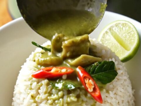A jade-green ceramic slow cooker filled with creamy Thai green coconut chicken curry topped with fresh basil.