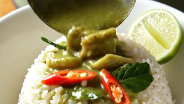 A jade-green ceramic slow cooker filled with creamy Thai green coconut chicken curry topped with fresh basil.