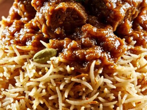 A close-up of a ruby ceramic slow cooker filled with tender Kashmiri Lamb Rogan Josh featuring a rich crimson gravy.