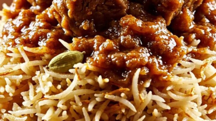 A close-up of a ruby ceramic slow cooker filled with tender Kashmiri Lamb Rogan Josh featuring a rich crimson gravy.