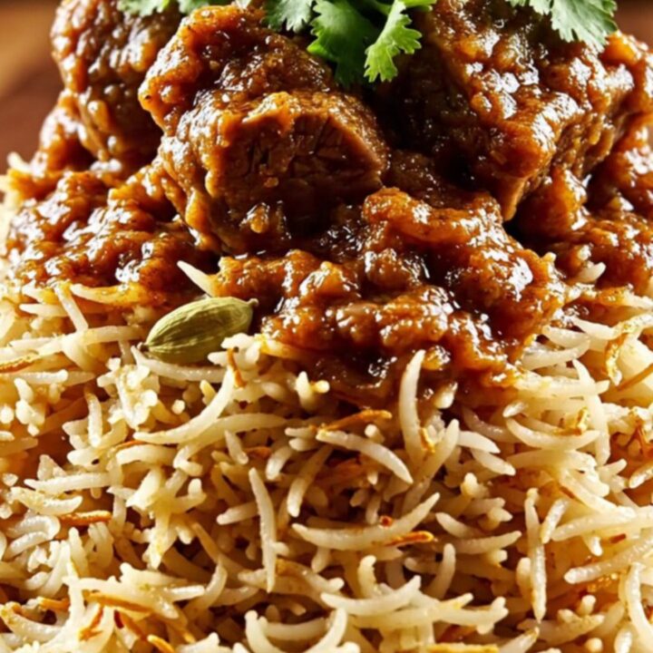 A close-up of a ruby ceramic slow cooker filled with tender Kashmiri Lamb Rogan Josh featuring a rich crimson gravy.