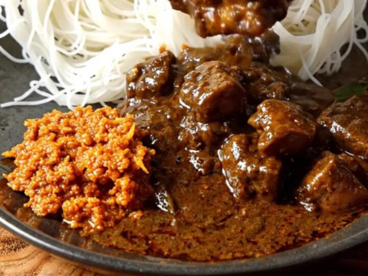 A close-up of a dark, aromatic Sri Lankan black pork curry served in a ceramic bowl with tender meat.