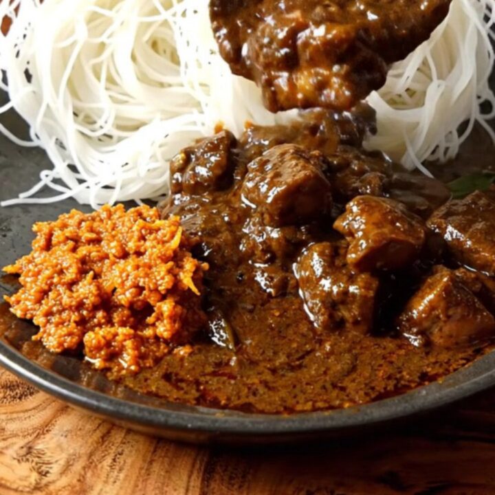 A close-up of a dark, aromatic Sri Lankan black pork curry served in a ceramic bowl with tender meat.
