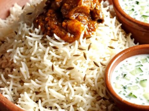 A close-up view of fiery Goan Pork Vindaloo in a ruby ceramic crockpot with a rich red sauce.