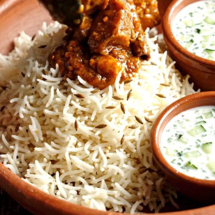 A close-up view of fiery Goan Pork Vindaloo in a ruby ceramic crockpot with a rich red sauce.