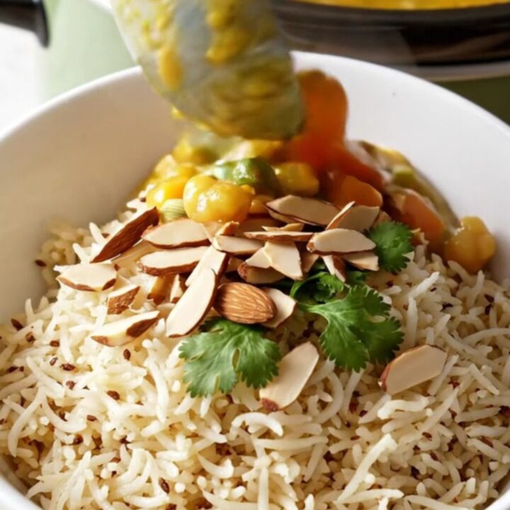 A close-up of a bowl of creamy Vegetable Korma served over basmati rice with almonds and cilantro.