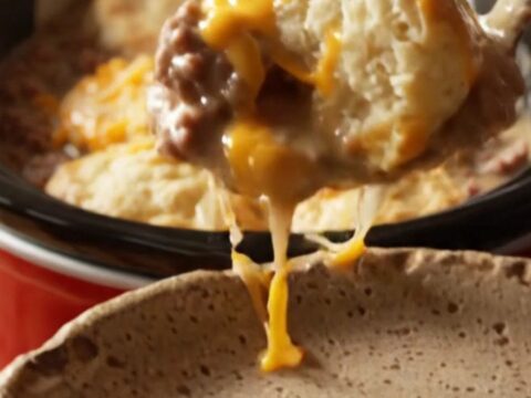 A close-up view of the finished breakfast bake showing golden fluffy biscuits and melted cheese in a red crockpot.