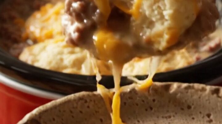 A close-up view of the finished breakfast bake showing golden fluffy biscuits and melted cheese in a red crockpot.