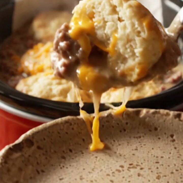 A close-up view of the finished breakfast bake showing golden fluffy biscuits and melted cheese in a red crockpot.
