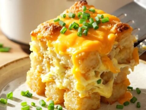 A warm, cheesy breakfast casserole in a white slow cooker, topped with crispy bacon and chives.