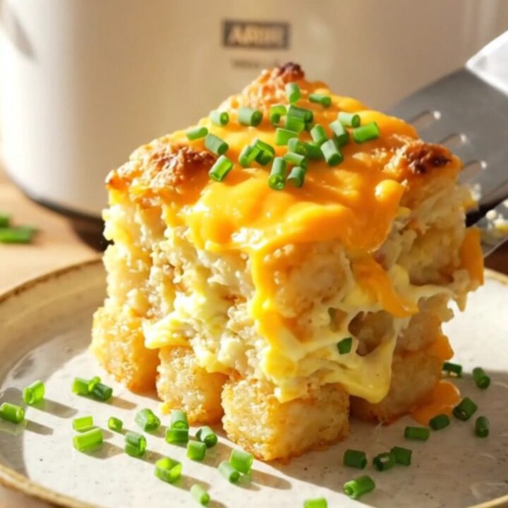 A warm, cheesy breakfast casserole in a white slow cooker, topped with crispy bacon and chives.