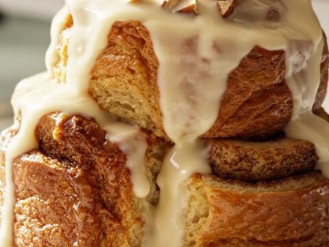 A warm, golden-brown cinnamon roll French toast casserole inside a ceramic Crockpot, topped with pecans.