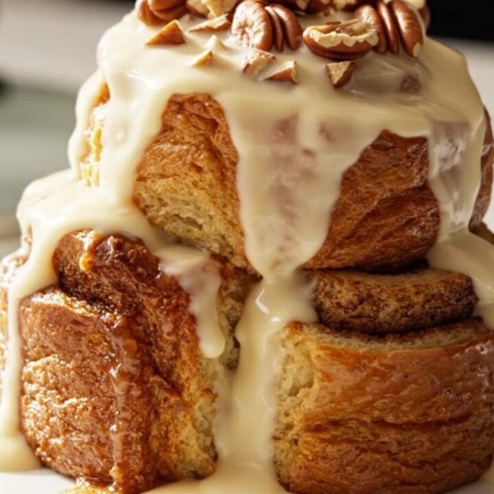 A warm, golden-brown cinnamon roll French toast casserole inside a ceramic Crockpot, topped with pecans.