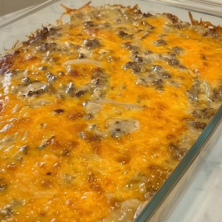 A fresh cheesy ground beef and potato casserole in a clear glass baking dish on a marble counter