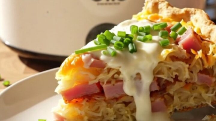 A close-up view of a cheesy hashbrown quiche in a white slow cooker with ham and Gruyere visible.