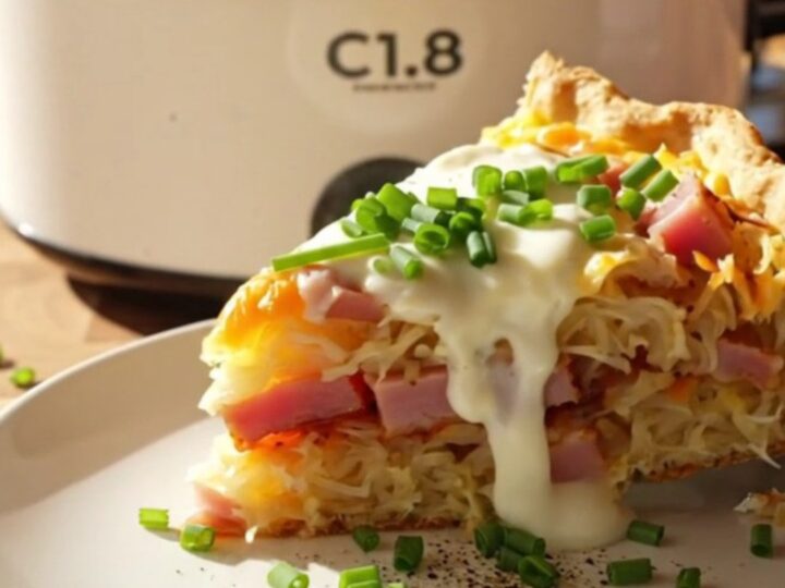 A close-up view of a cheesy hashbrown quiche in a white slow cooker with ham and Gruyere visible.