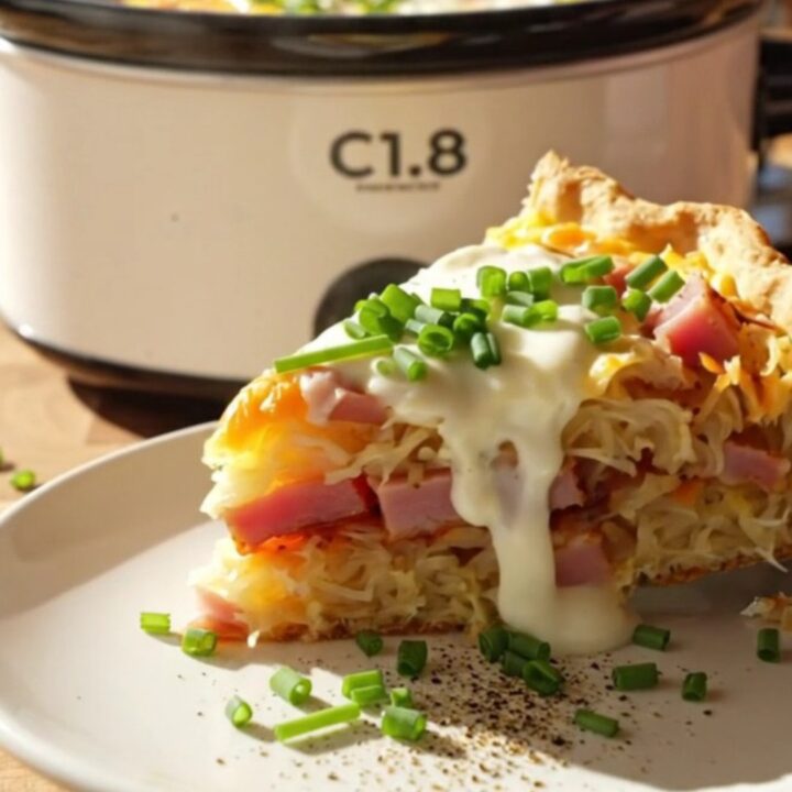 A close-up view of a cheesy hashbrown quiche in a white slow cooker with ham and Gruyere visible.