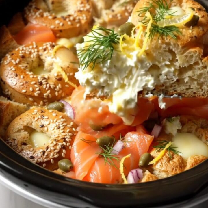 A close-up of a golden-brown everything bagel strata in a black crockpot, garnished with fresh dill and lemon zest.