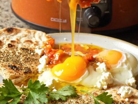 A rustic terracotta crockpot filled with vibrant red shakshuka and perfectly poached eggs.
