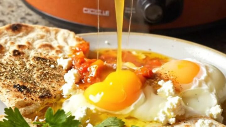 A rustic terracotta crockpot filled with vibrant red shakshuka and perfectly poached eggs.