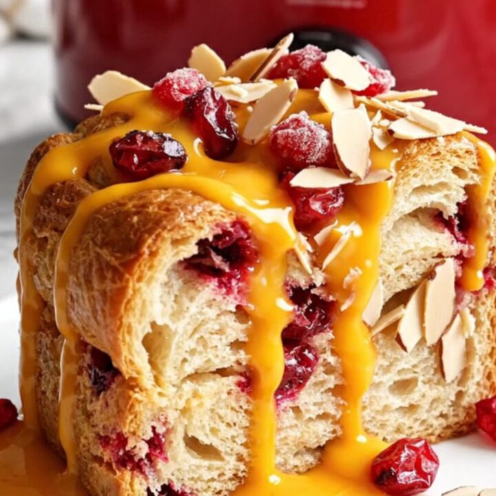 A festive cranberry orange brioche French toast casserole in a red Crockpot, topped with sugared cranberries and almonds.