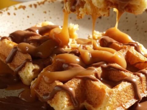A warm, golden-brown cinnamon sugar waffle casserole in a ceramic crockpot, drizzled with thick dulce de leche.