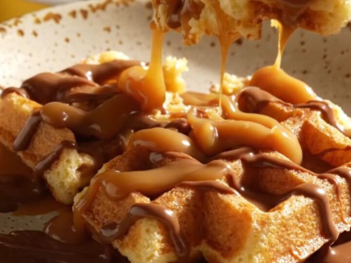 A warm, golden-brown cinnamon sugar waffle casserole in a ceramic crockpot, drizzled with thick dulce de leche.