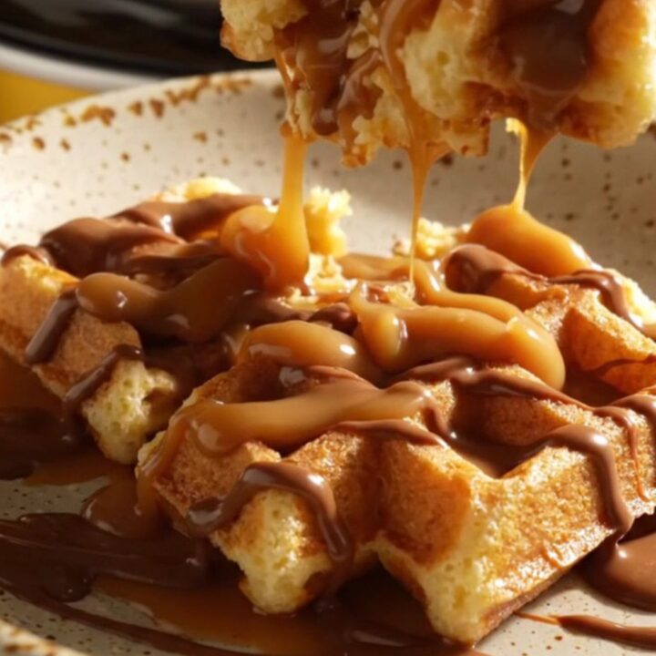 A warm, golden-brown cinnamon sugar waffle casserole in a ceramic crockpot, drizzled with thick dulce de leche.