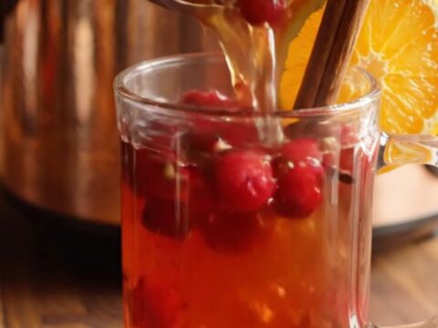 A gleaming copper crockpot filled with steaming mulled cider, garnished with blood orange wheels and cranberries.