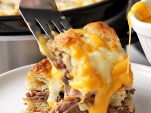 A close-up of a warm Philly cheesesteak breakfast strata in a slow cooker with melted cheese.