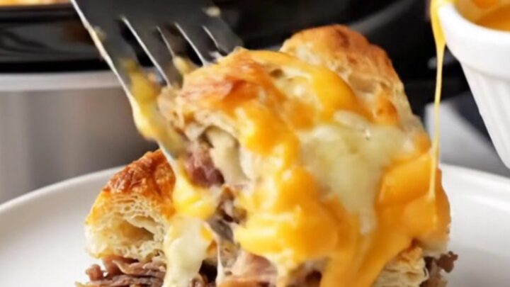 A close-up of a warm Philly cheesesteak breakfast strata in a slow cooker with melted cheese.