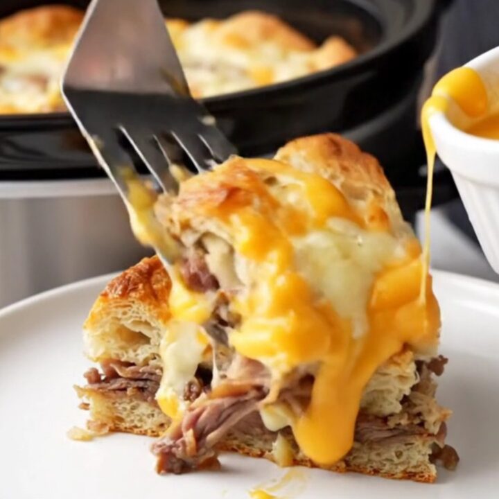 A close-up of a warm Philly cheesesteak breakfast strata in a slow cooker with melted cheese.
