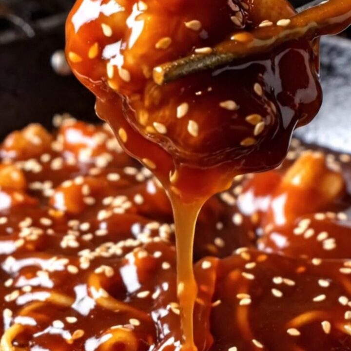 Glossy sweet-and-sour sesame chicken chunks over a golden crispy-bottom chow mein noodle cake with toasted sesame seeds