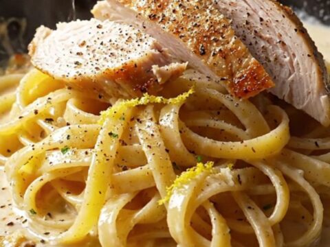 A fork twirling fettuccine coated in creamy lemon garlic sauce, topped with sliced chicken and parsley.
