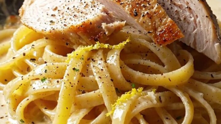 A fork twirling fettuccine coated in creamy lemon garlic sauce, topped with sliced chicken and parsley.