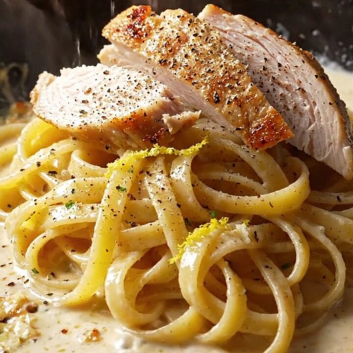 A fork twirling fettuccine coated in creamy lemon garlic sauce, topped with sliced chicken and parsley.
