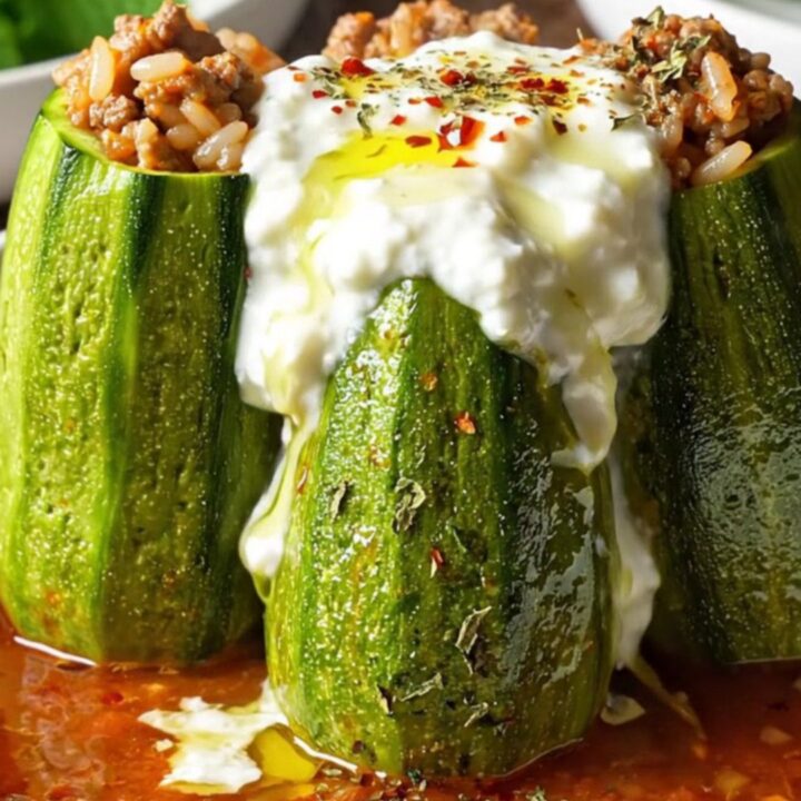 Stuffed round zucchini in a Dutch oven with garlic tomato sauce, topped with yogurt and red pepper oil
