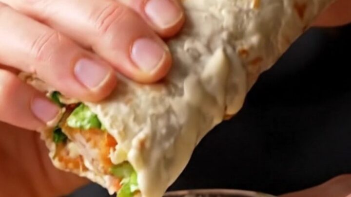 Golden toasted chicken Caesar wrap sliced diagonally, showing layers of crispy chicken, romaine, and parmesan.